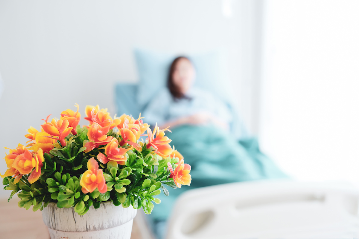 A woman in a hospital bed looks at a pot of flowers