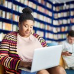 A Black woman works on her laptop in a library