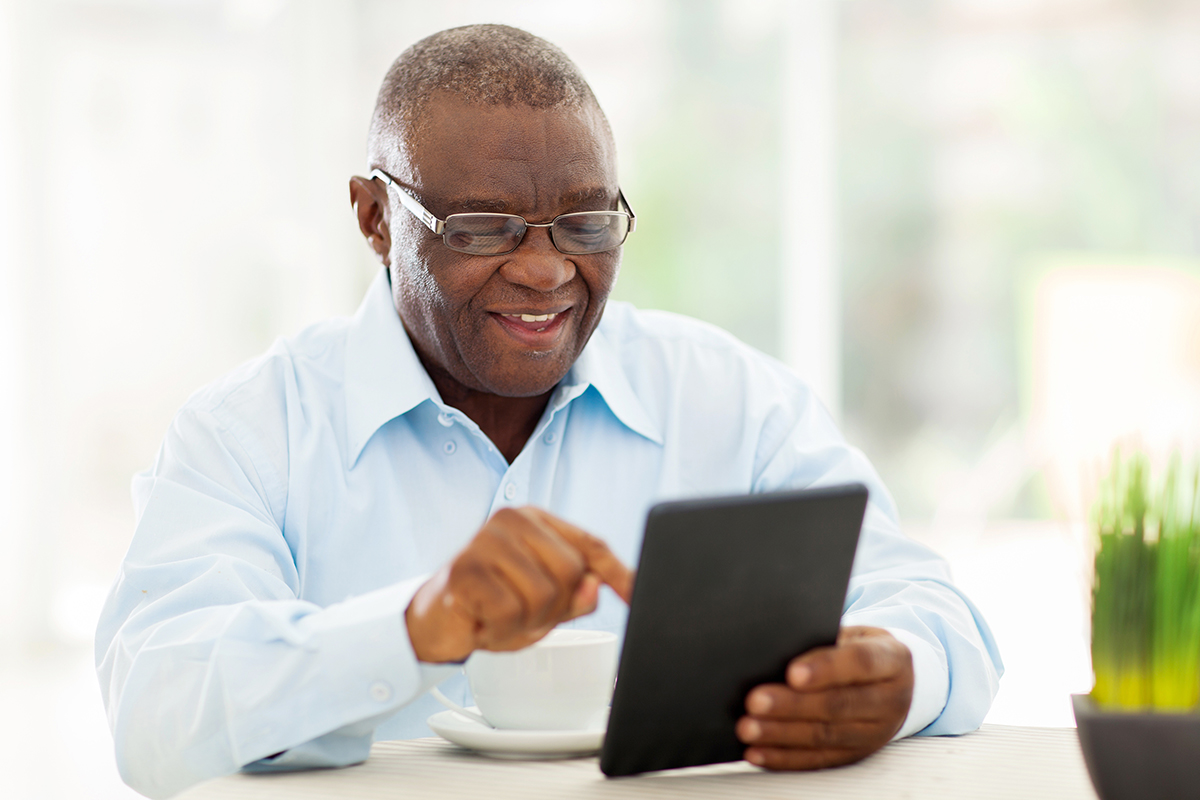 A senior Black man uses a tablet at his dining room table
