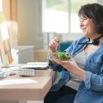 A woman eats a salad while attending an online meeting