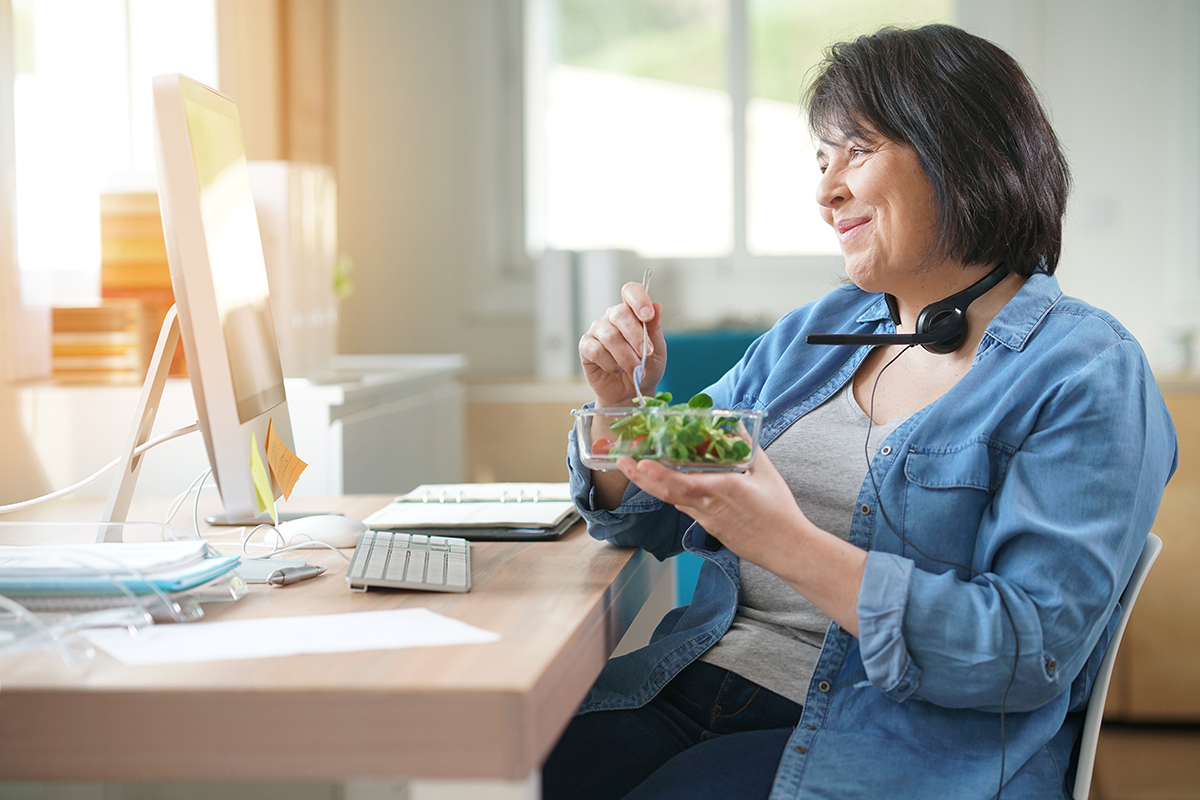 A woman eats a salad while attending an online meeting