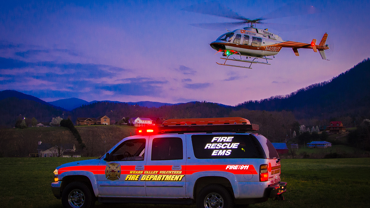 EMS truck with lights on sits in front of hovering emergency rescue helicopter